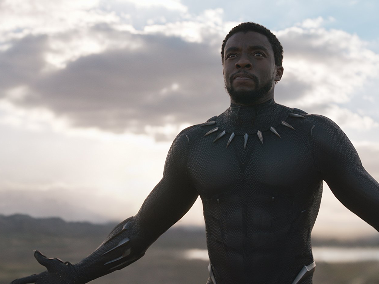 King T'challa wearing the Black Panther suit without his helmet stands with his arms stretched wipe open, looking upwards