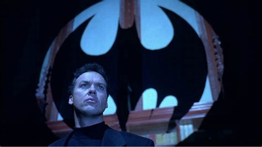 Batman looking into the distance as the batsignal hangs behind him